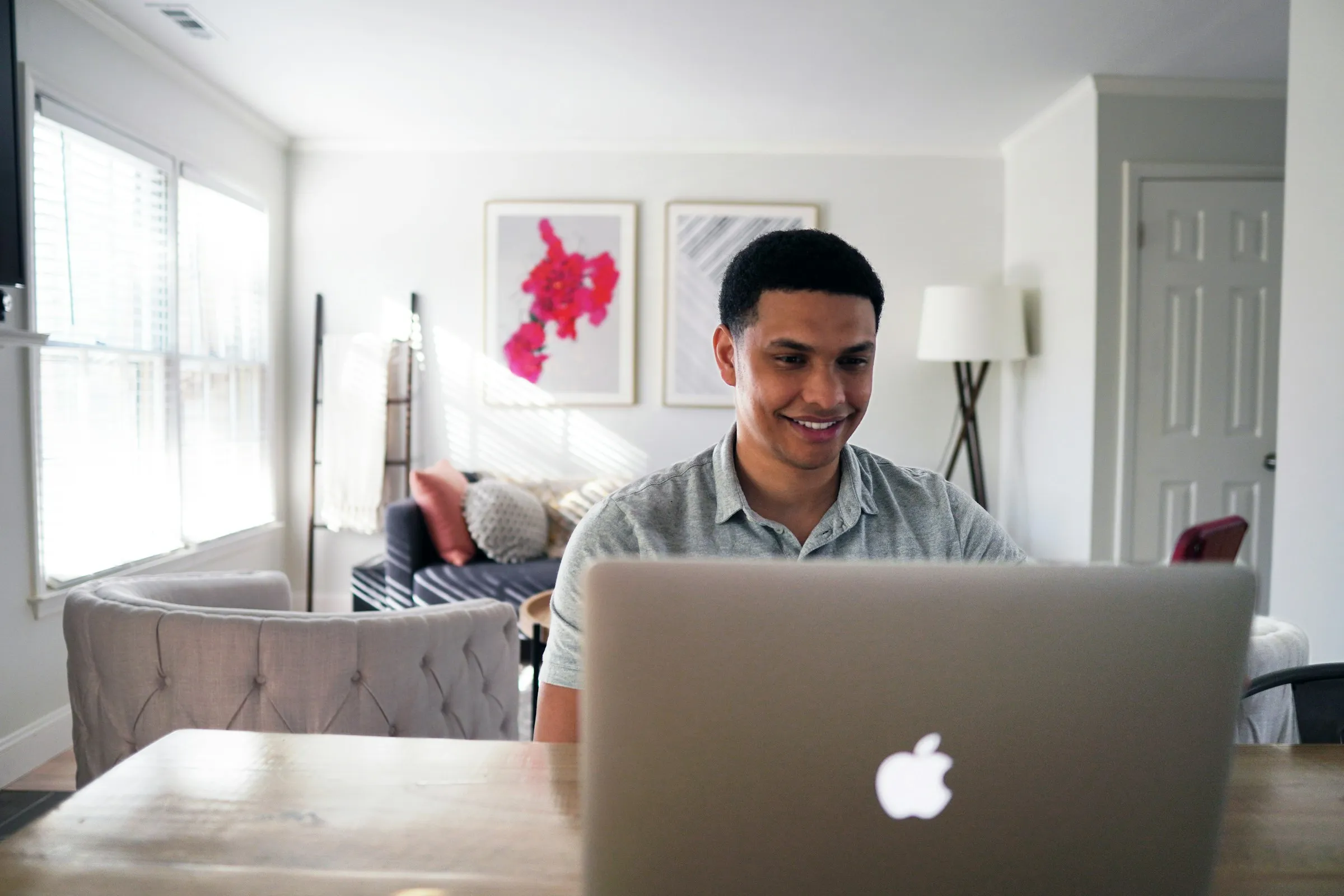 Homem sorrindo enquanto trabalha em um notebook na mesa de uma sala clara