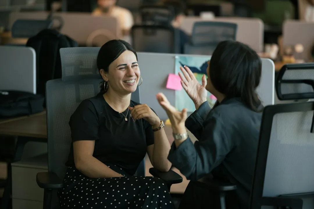 Duas pessoas conversando em um escritório, uma delas sorrindo, em meio à rotina de trabalho